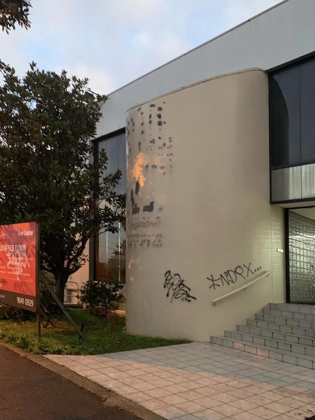 Curved stair tower before, stained cream render covered in graffiti, Footscray