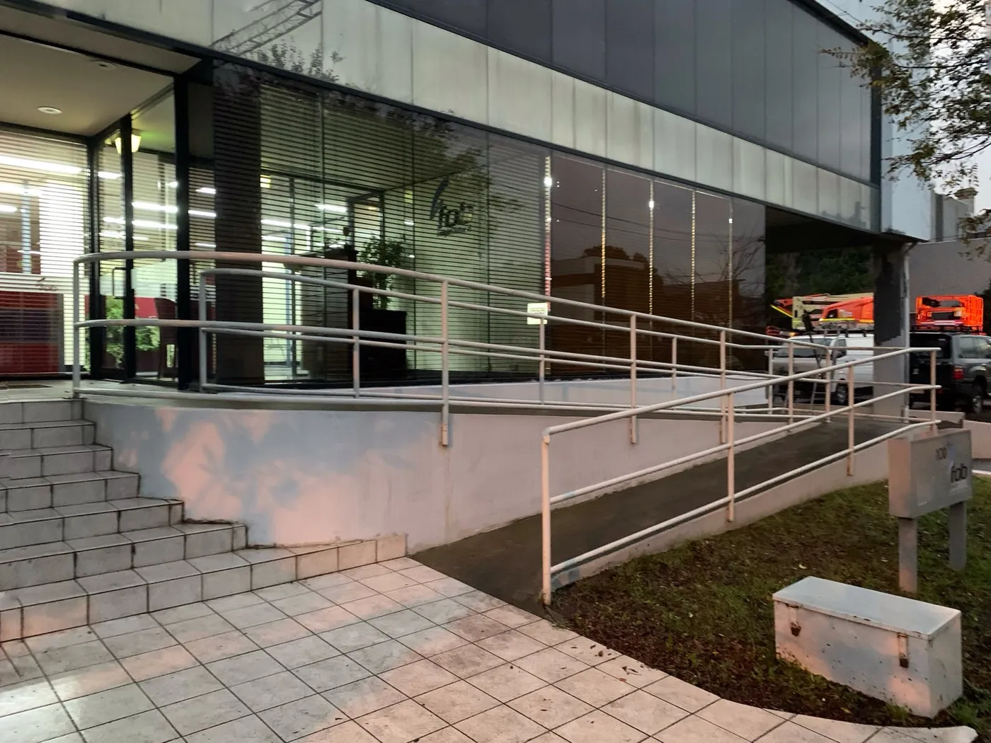 Office building entrance before, pale render around the glazed frontage with steps and access ramp, Footscray