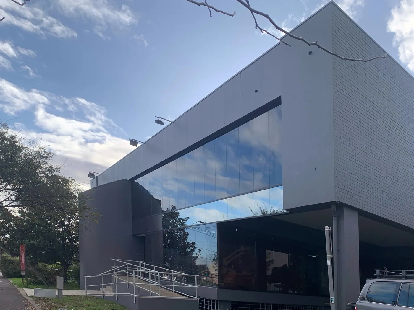 Full street elevation finished, charcoal walls under a long band of reflective glazing, Footscray