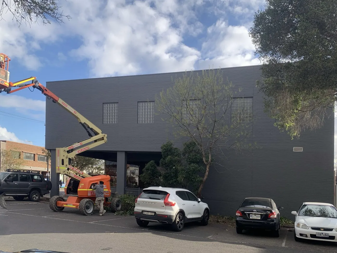 Boom lift working the upper wall of the office building above the occupied car park, Footscray
