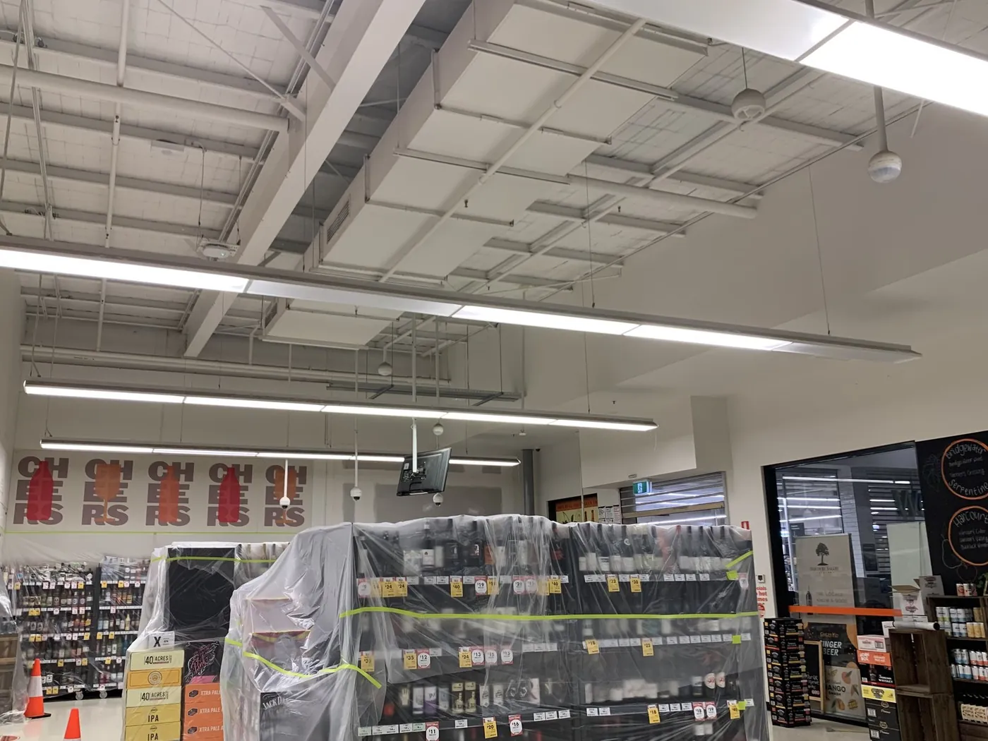 Bottle shop open ceiling before, white structure and ducting on show, stock wrapped in plastic, Ballarat