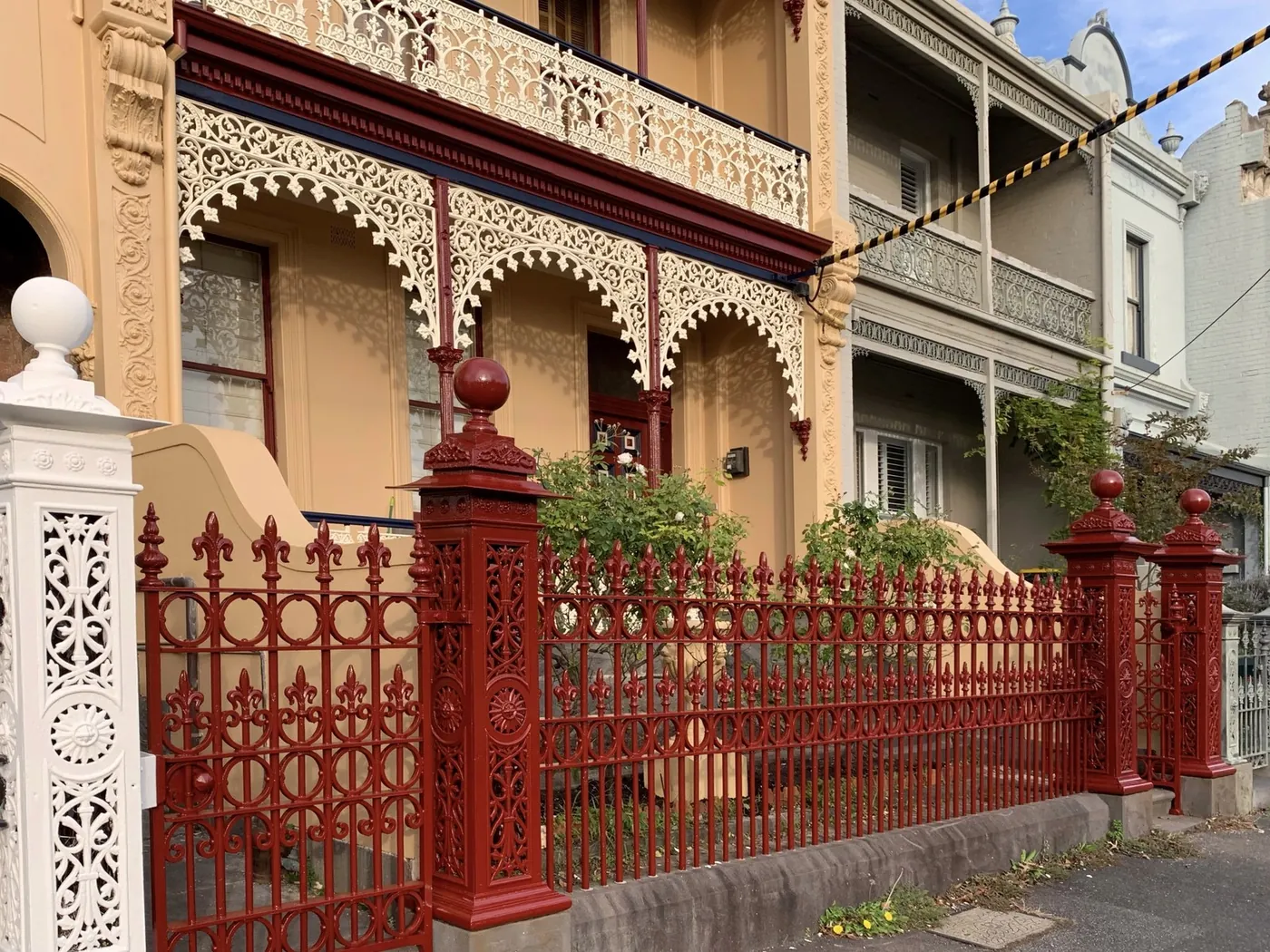 Freshly painted Victorian terrace in Melbourne, ochre render, cream cast iron lace and a deep red front fence, Carlton