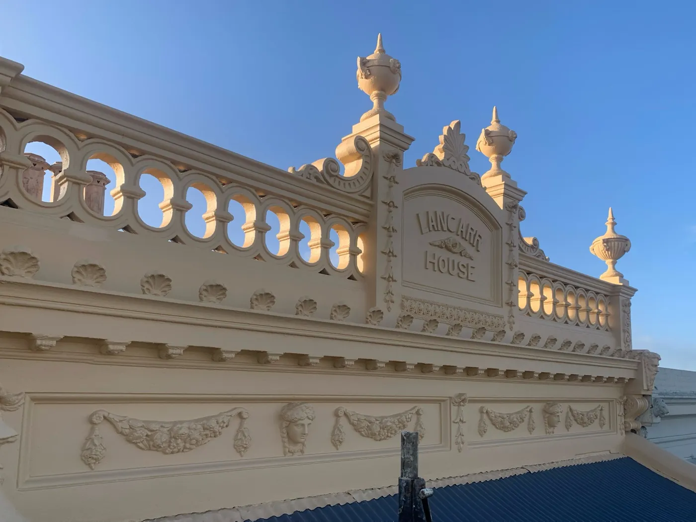 Ornate rendered parapet with the LANCARR HOUSE nameplate, urns and balustrade in heritage cream against a blue sky, Carlton
