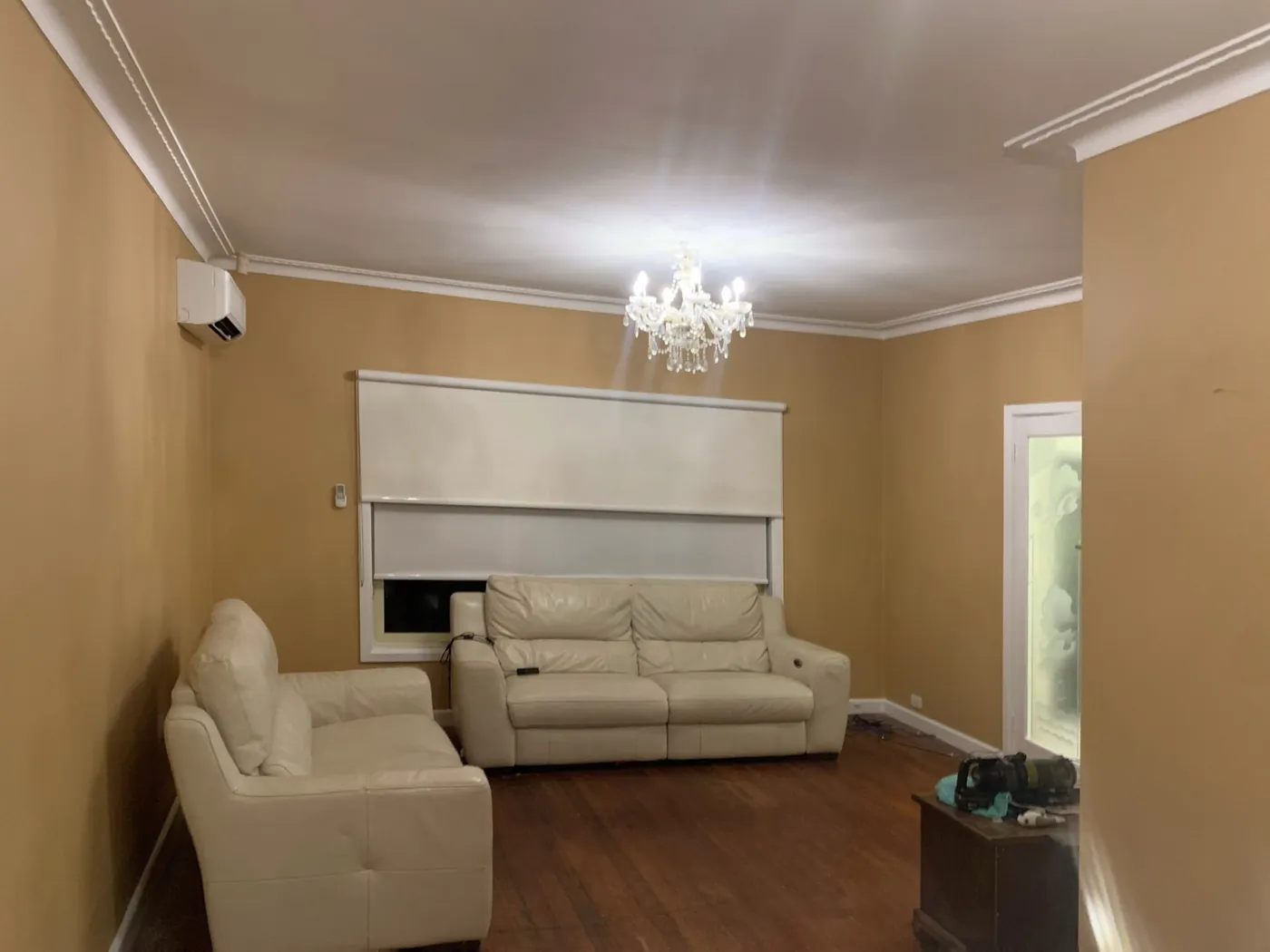 Finished lounge in warm apricot with a crystal chandelier, white cornice and timber floor, Oakleigh
