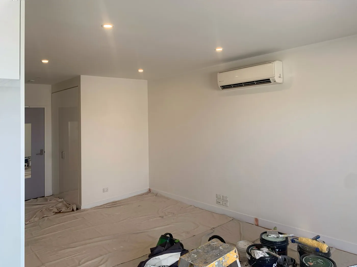Apartment living room part way through, white walls with drop sheets and paint tins on the floor, Preston