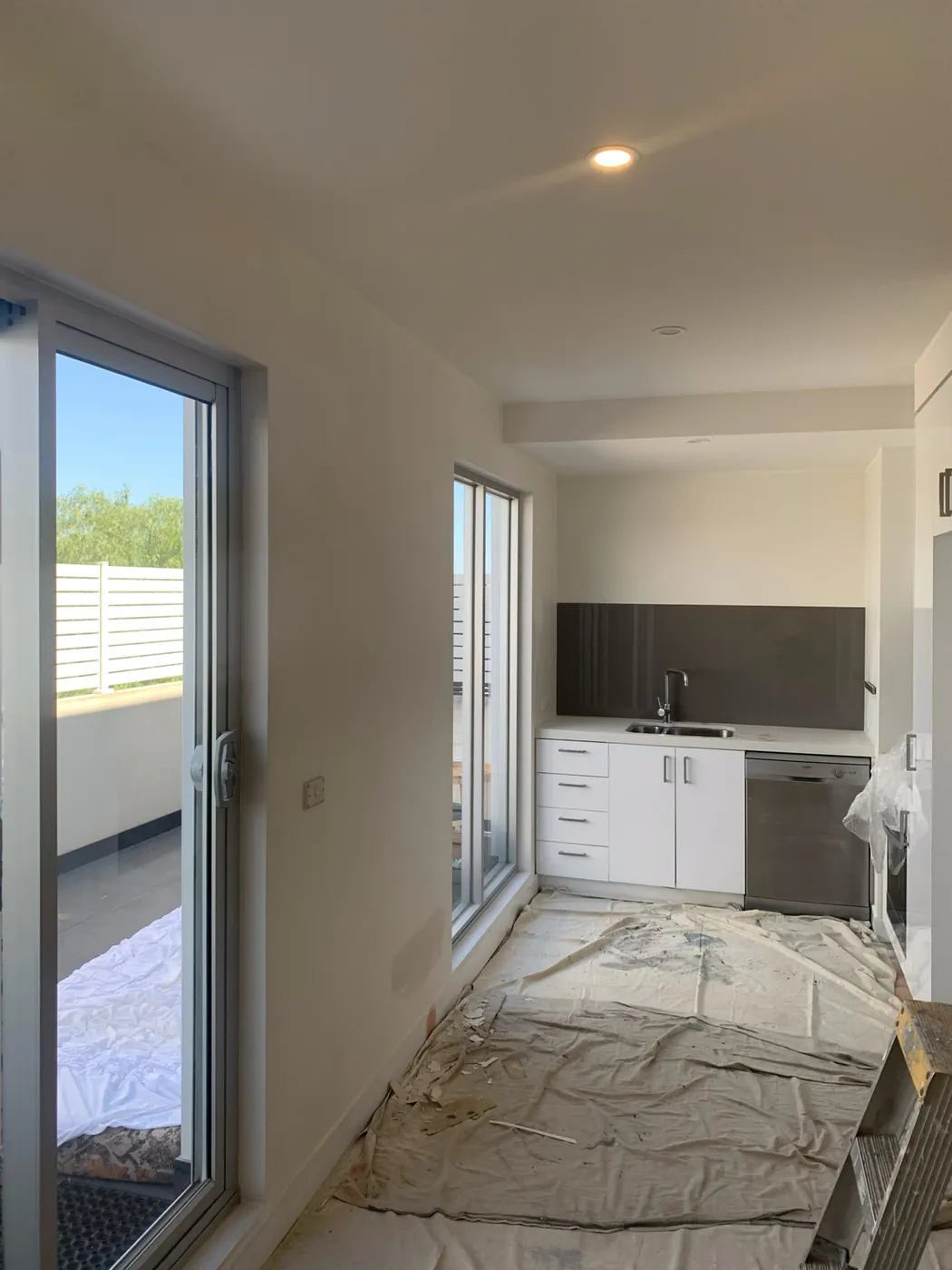 Apartment kitchen part way through, drop sheets over the floor beside the black splashback, Preston