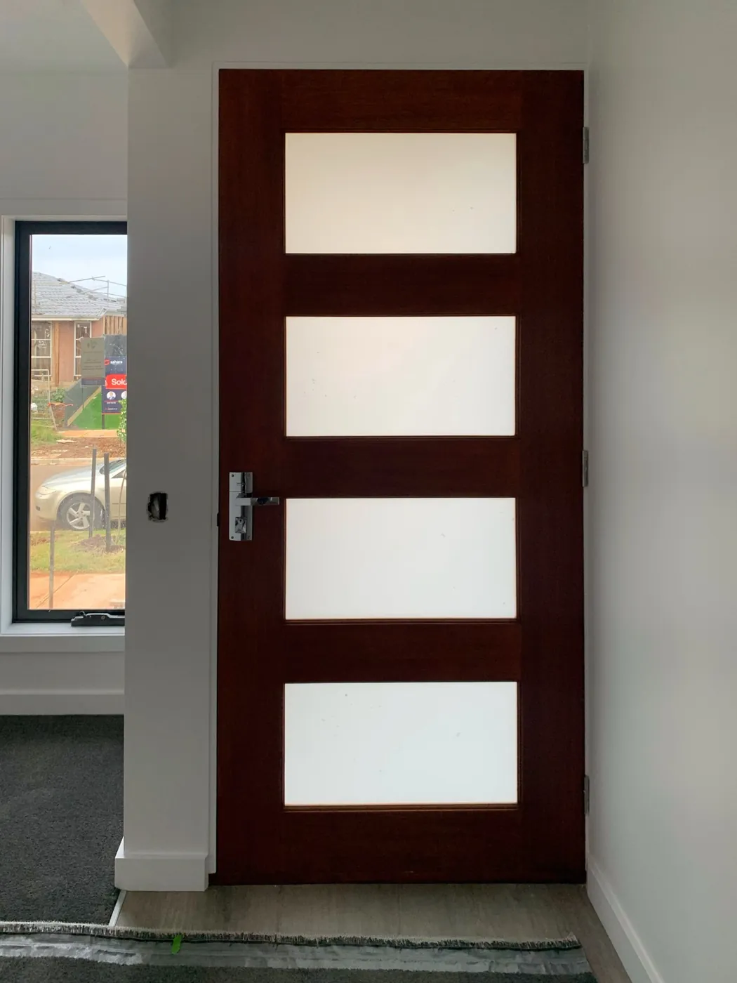 Entrance of a new home, stained timber front door framed by freshly painted walls and architraves, Melton