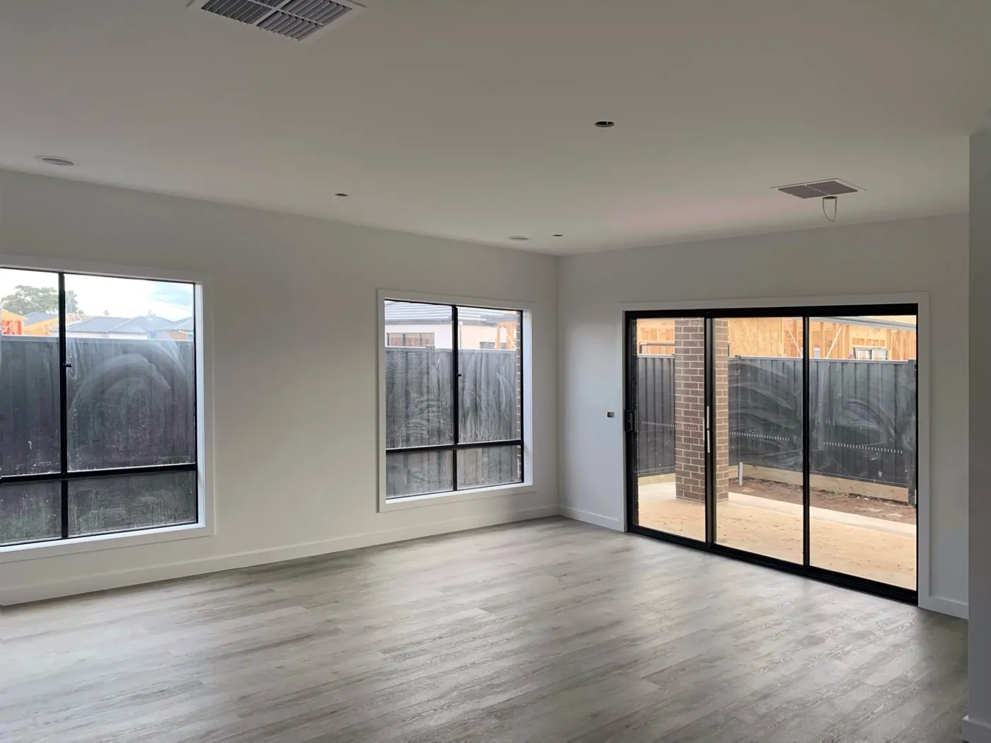 Empty living room of a new build in Melton, Melbourne, painted before handover, with the neighbouring house still in