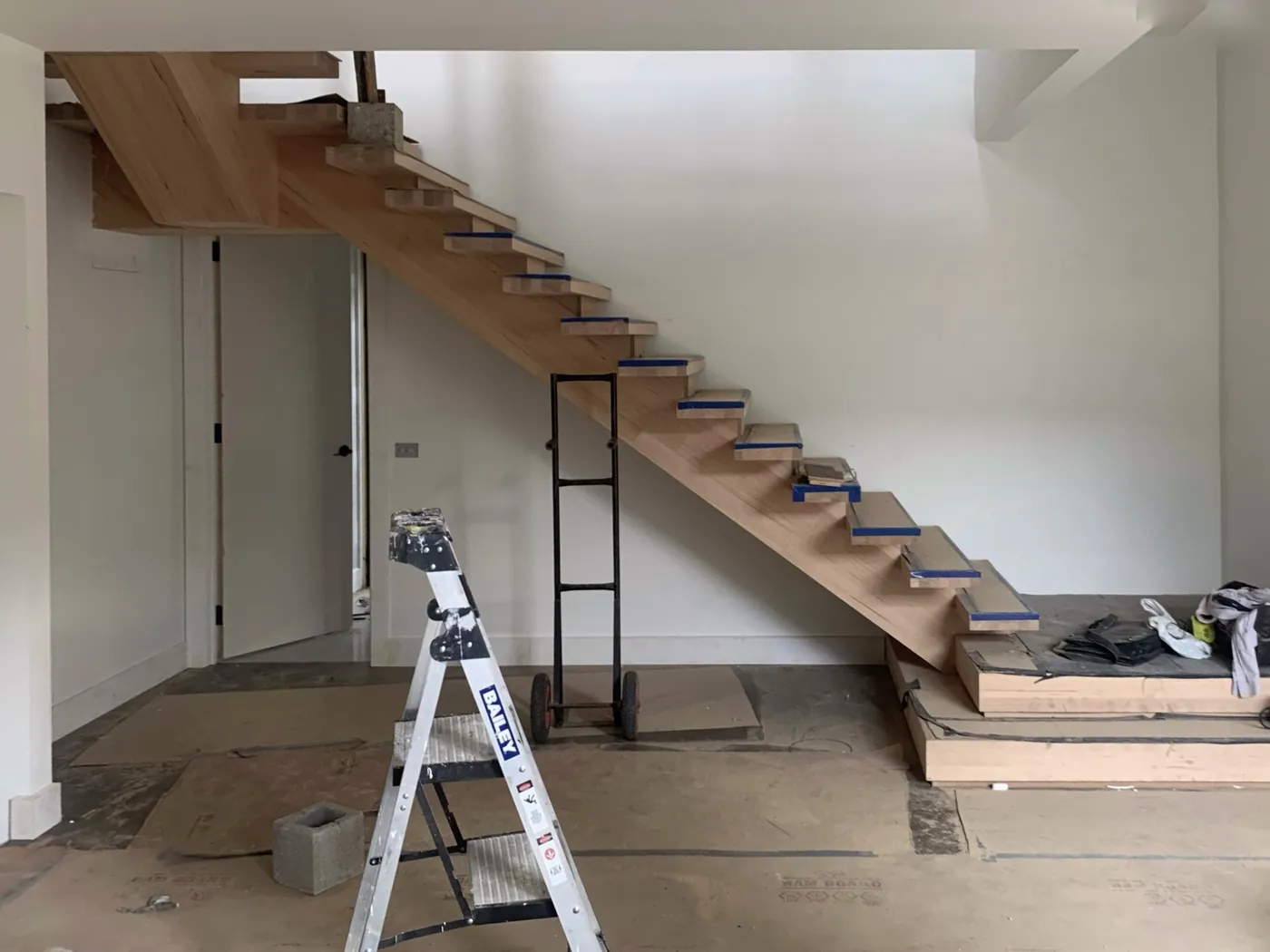Floating staircase before, bare hardwood treads with blue masking tape along the edges and a ladder alongside, Doncaster