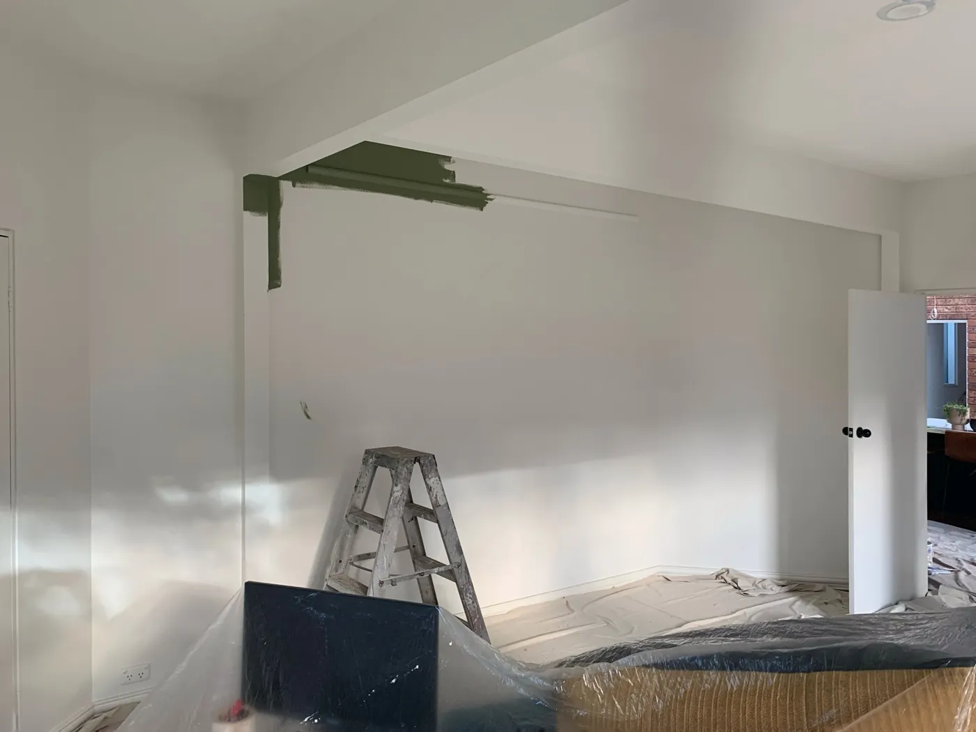 Living room part way through, white walls with the bulkhead already in olive, ladder and drop sheets, Ferntree Gully