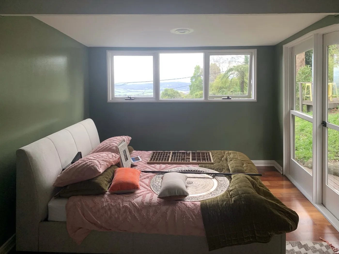 Bedroom in deep olive green looking out over the valley through a wide window, timber floor and glazed door, Ferntree Gully