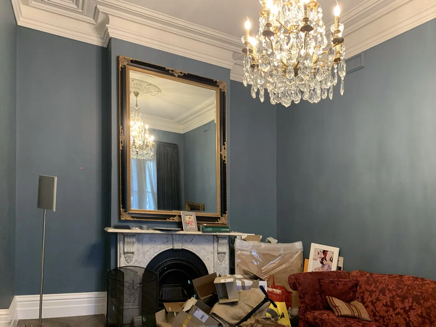 Blue grey room with a marble fireplace, gilt mirror and crystal chandelier under a white cornice, St Kilda