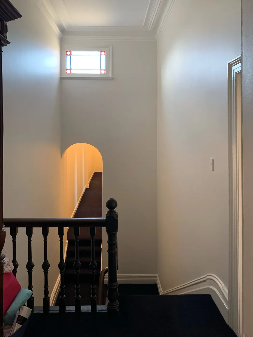 Stair hall with an arched opening, black timber balustrade and coloured glass window above the landing, St Kilda