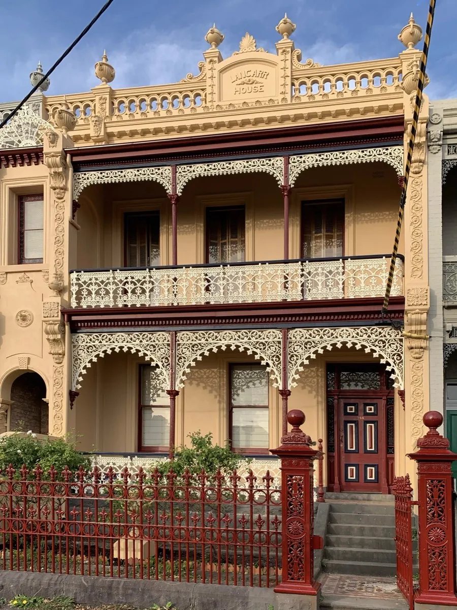 Victorian terrace facade in Melbourne after repainting, ochre render with cream cast iron lace, Carlton